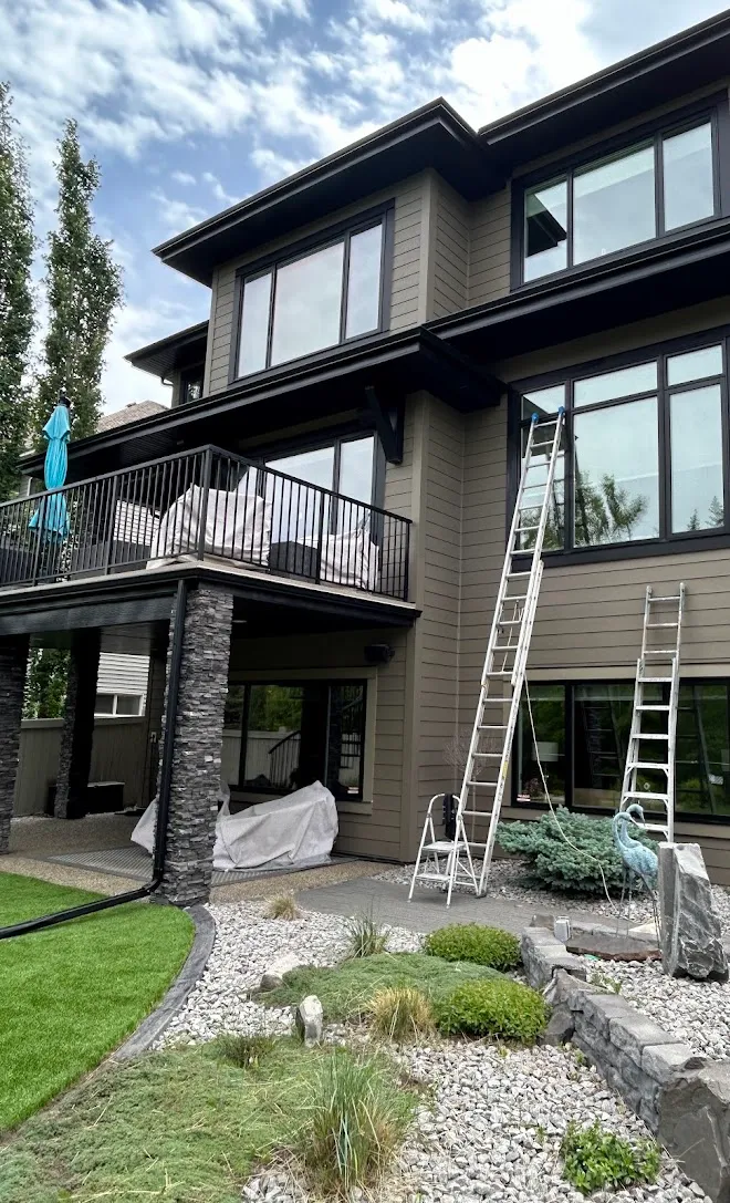 Crew ladders set against a large home during an exterior repaint — Leonard’s Painting, Edmonton area