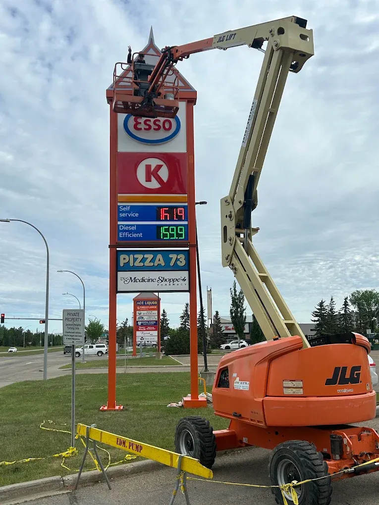 JLG boom lift beside a tall roadside sign during repainting — Leonard’s Painting, Edmonton area